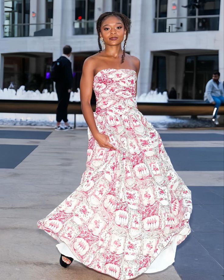 a woman in a white and pink dress standing on the sidewalk