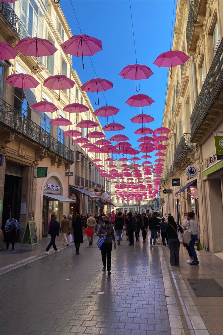 many pink umbrellas are hanging from the ceiling in this shopping area as people walk by