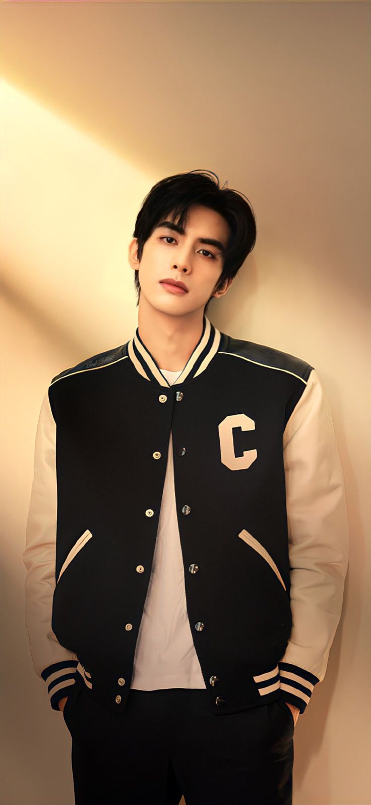 a young man wearing a black and white baseball jacket standing in front of a wall