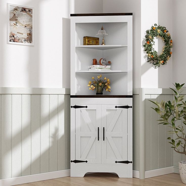 a white cabinet with doors and shelves in the corner next to a potted plant