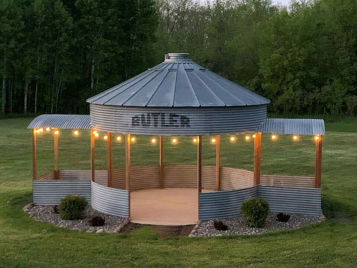 a round metal structure with lights on it in the middle of some grass and trees