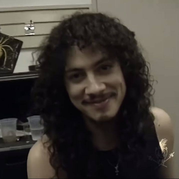 a man with long curly hair is smiling at the camera in front of a mirror