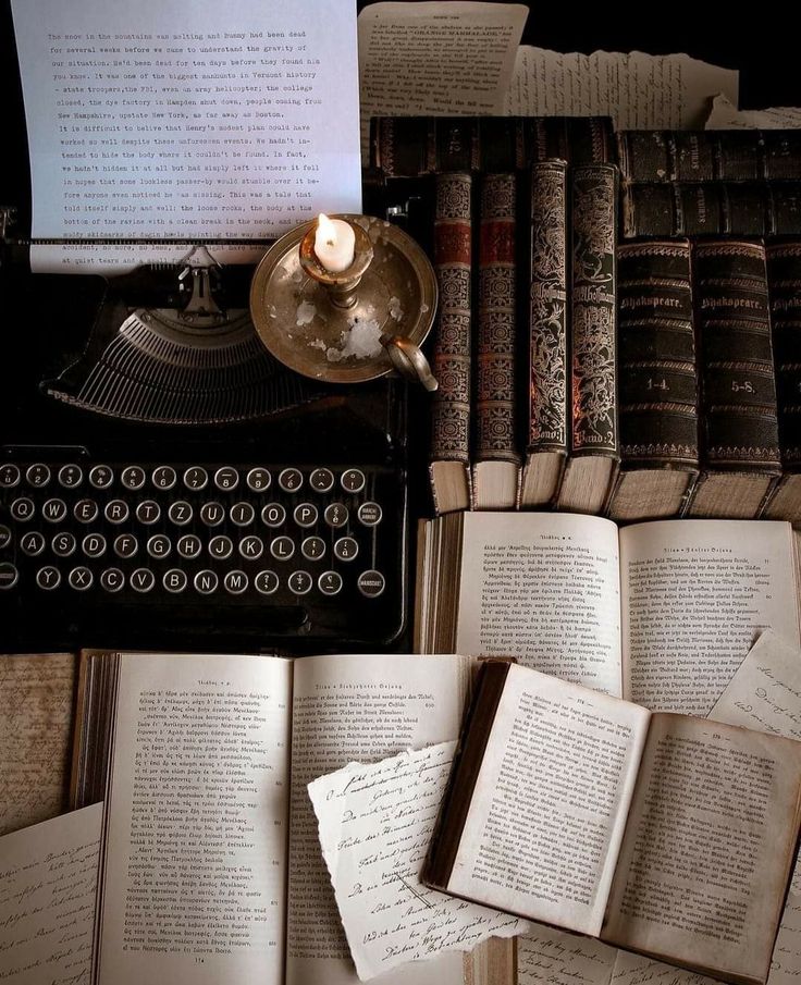 an old fashioned typewriter surrounded by books and paper with writing on it, next to a lit candle