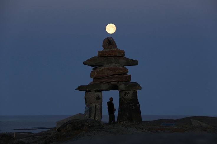 the full moon is setting over some rocks and a man standing in front of it