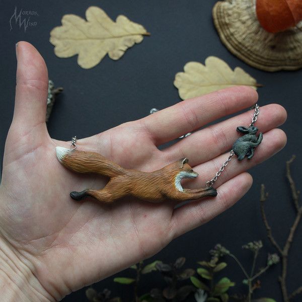 a hand holding a tiny animal necklace on it's palm, with leaves in the background