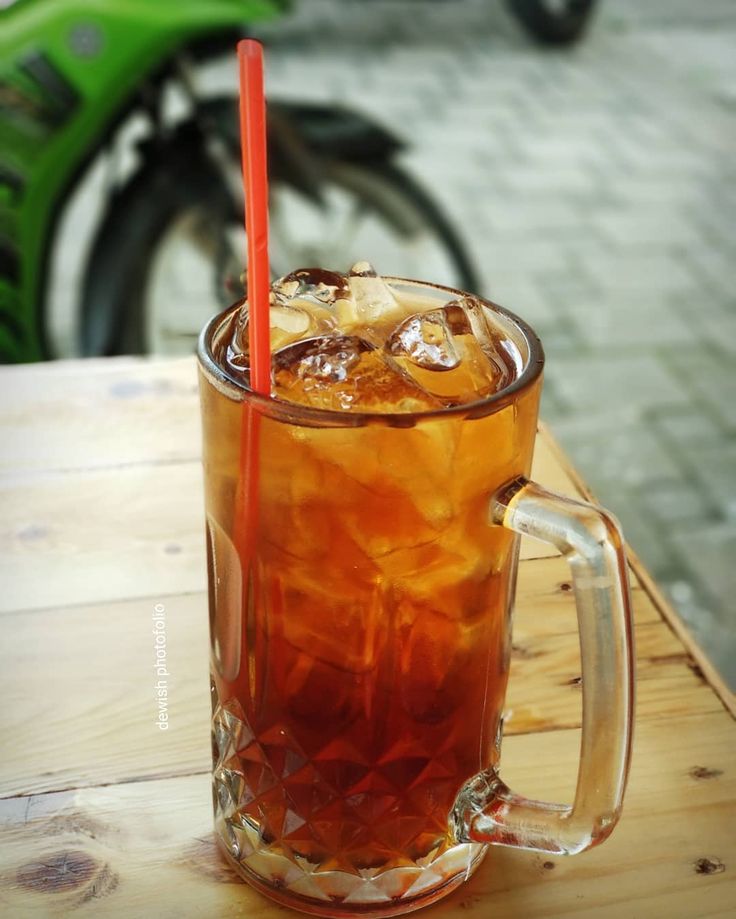 there is a glass with ice and a straw in it on the table next to a motorcycle