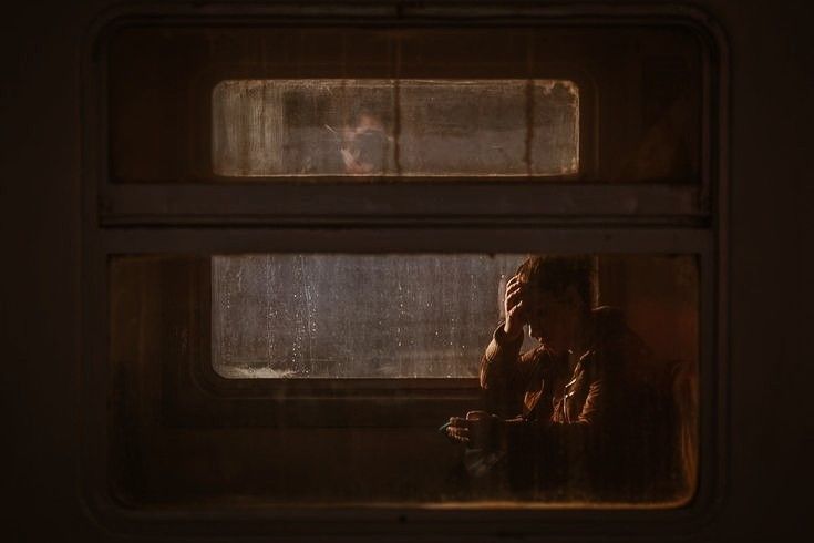 a person sitting on a train looking out the window at another person in the distance