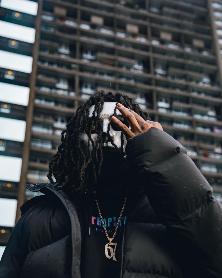 a man with dreadlocks covering his face while standing in front of a tall building