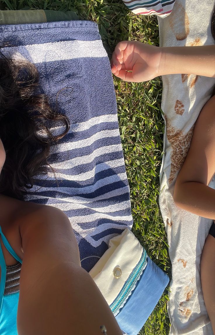 two women laying on the grass with towels around them and one woman holding her hand out