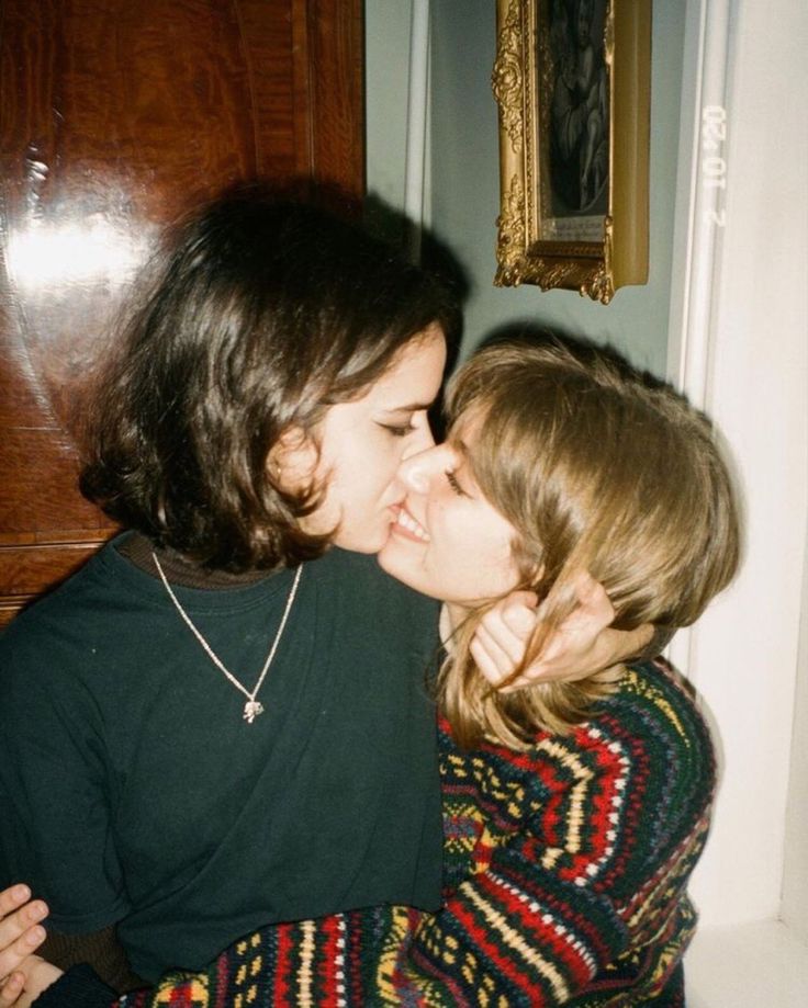 two women are kissing each other in front of a wooden door with a painting on the wall behind them