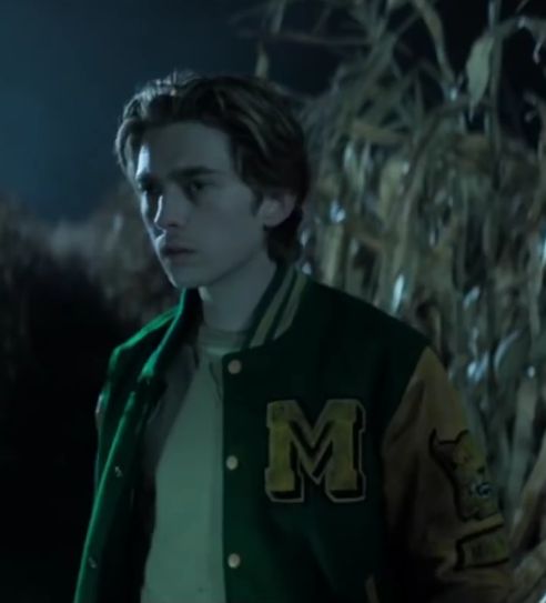 a young man standing in front of a cornfield at night wearing a green and yellow jacket