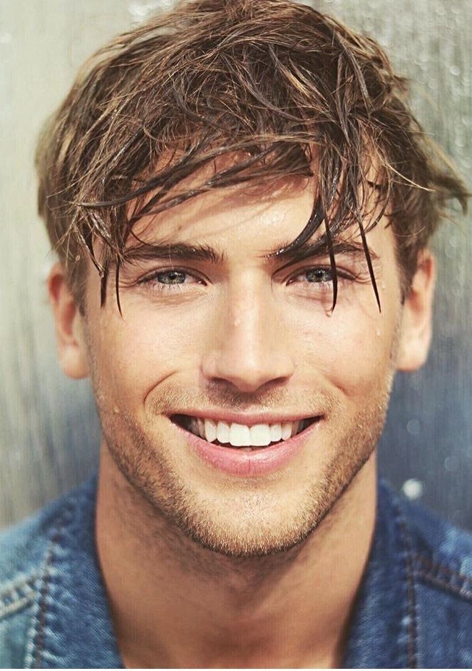 a close up of a person wearing a denim jacket and smiling at the camera with long hair on his head