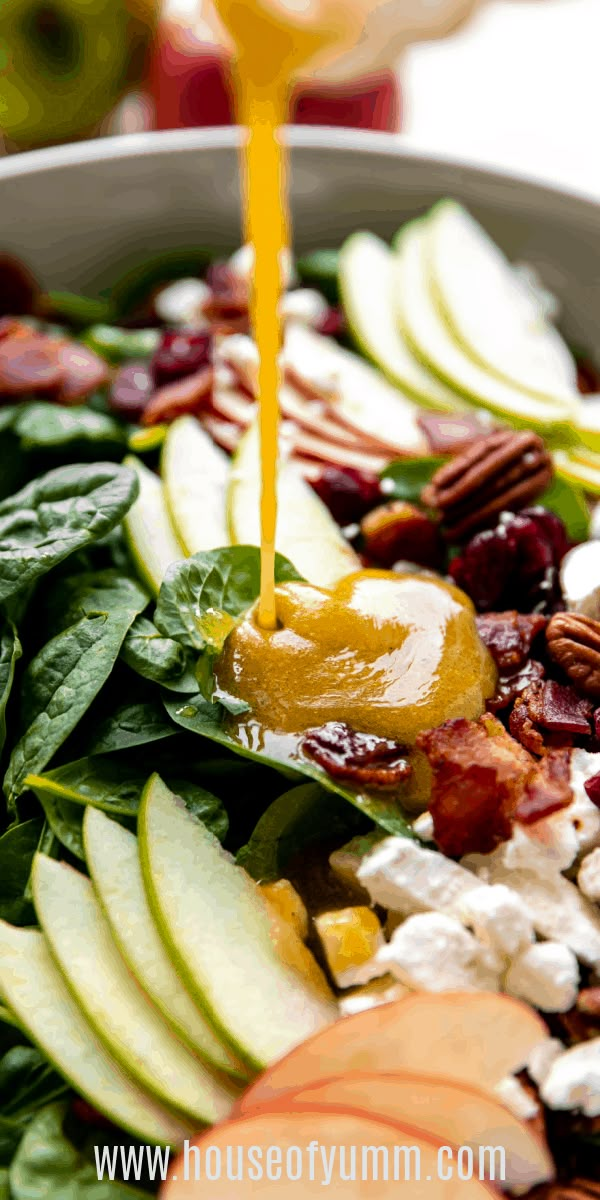 someone pouring dressing onto a salad with apples, spinach and pecans in the background