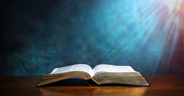 an open book sitting on top of a wooden table under a bright beam of light