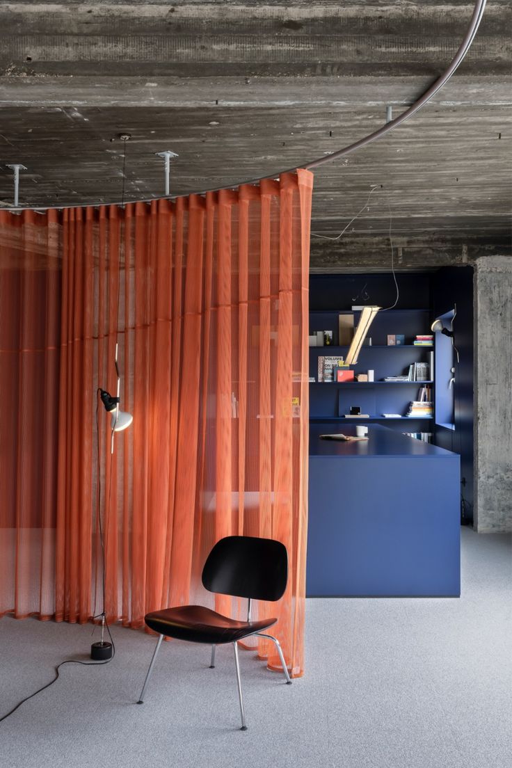 an orange curtain in the corner of a room with a black chair and bookshelf