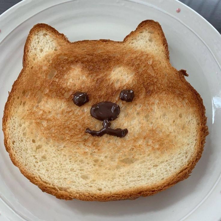 a toasted bread with a bear face drawn on it's side, sitting on a white plate