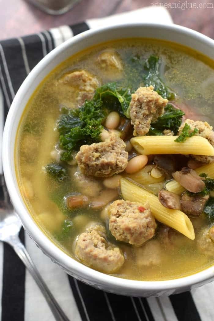 a bowl of soup with meatballs, pasta and spinach is on the table