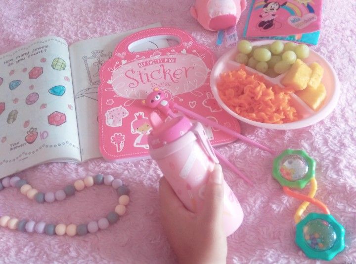 a child's hand is holding a pink bottle with candy and other items on it