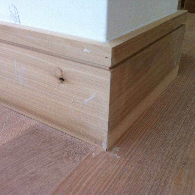 a wooden box sitting on top of a hard wood floor next to a white wall