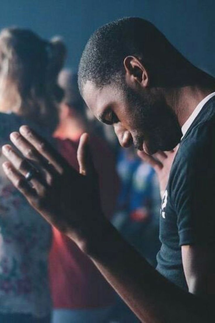 a man with his hands folded in front of him while others stand behind him and pray