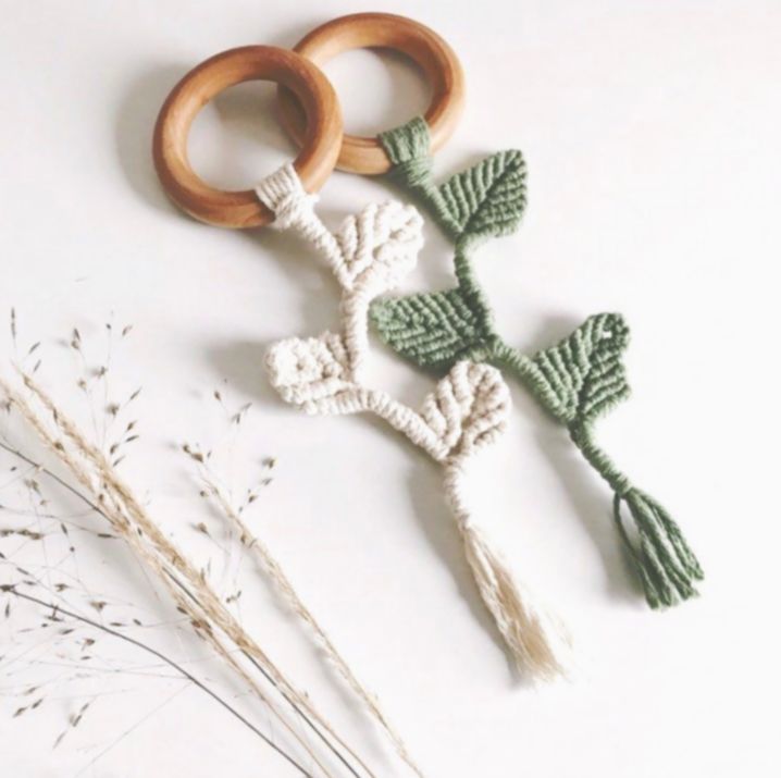 two crocheted wooden rings and some flowers on a white surface next to dried grass