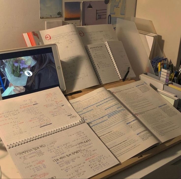 an open laptop computer sitting on top of a wooden desk covered in notebooks and papers