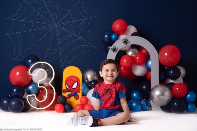 a young boy sitting on the floor in front of balloons and spider - man decorations