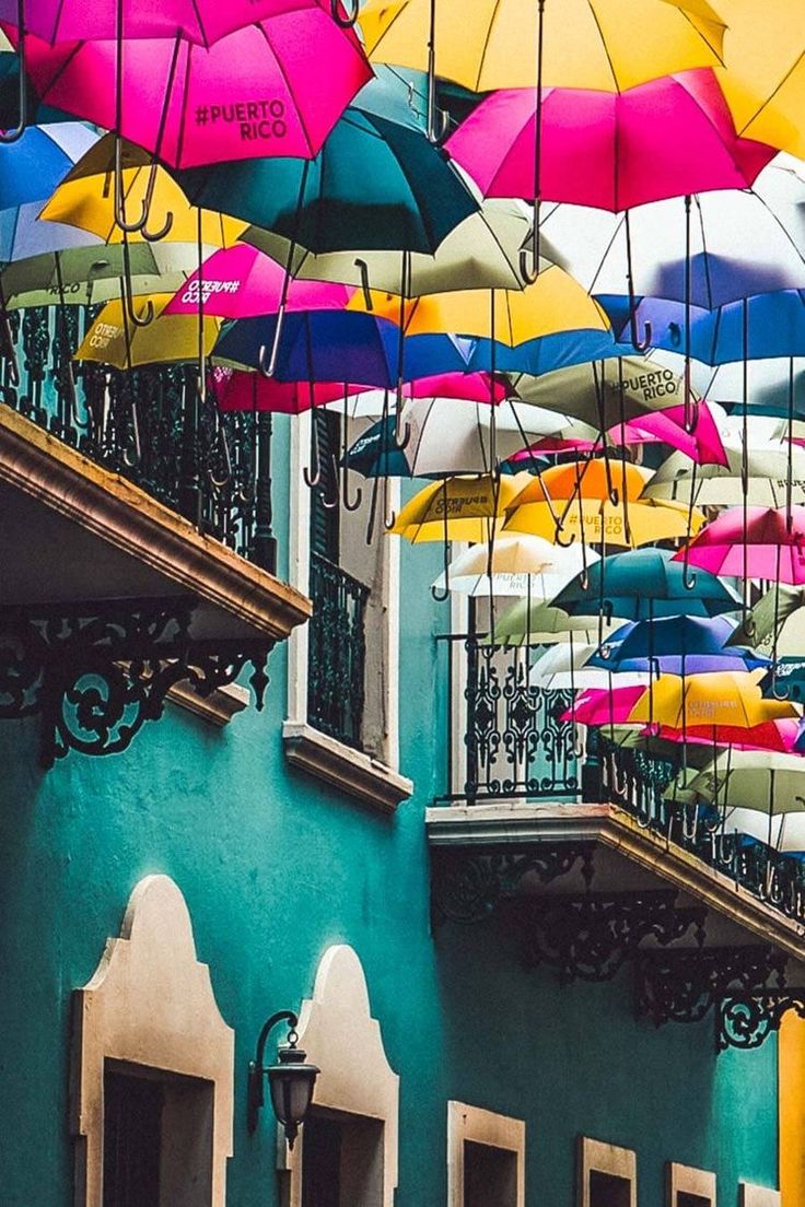 many colorful umbrellas hanging from the side of buildings