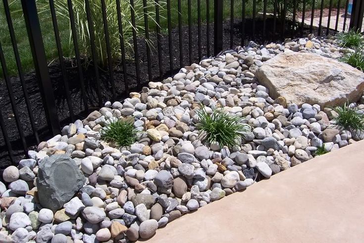 a rock garden with grass and rocks in the ground next to a black iron fence