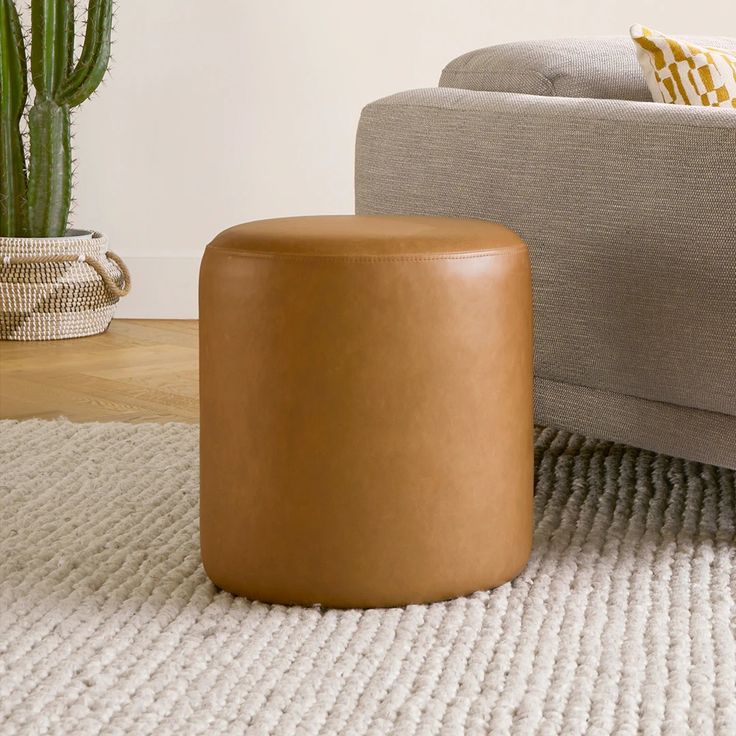 a brown leather stool sitting on top of a white rug next to a gray couch