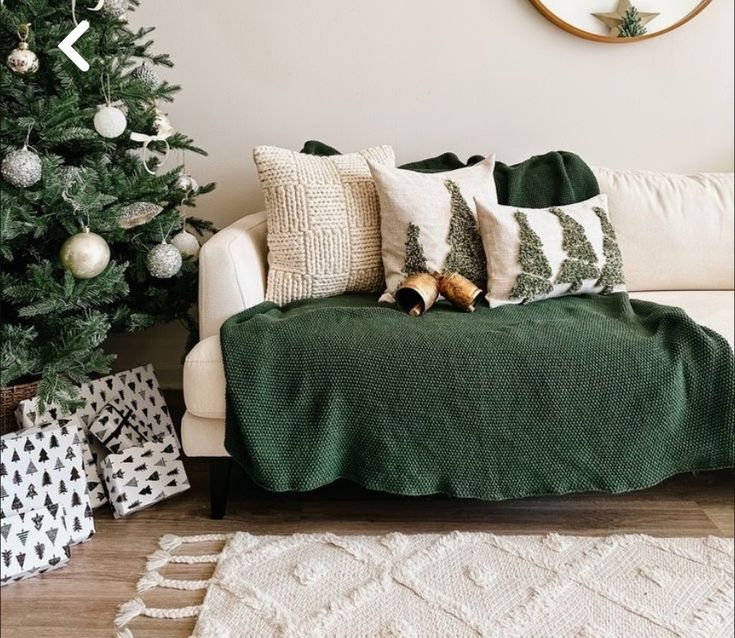 a christmas tree is next to a couch with pillows and blankets on it, along with other holiday decorations