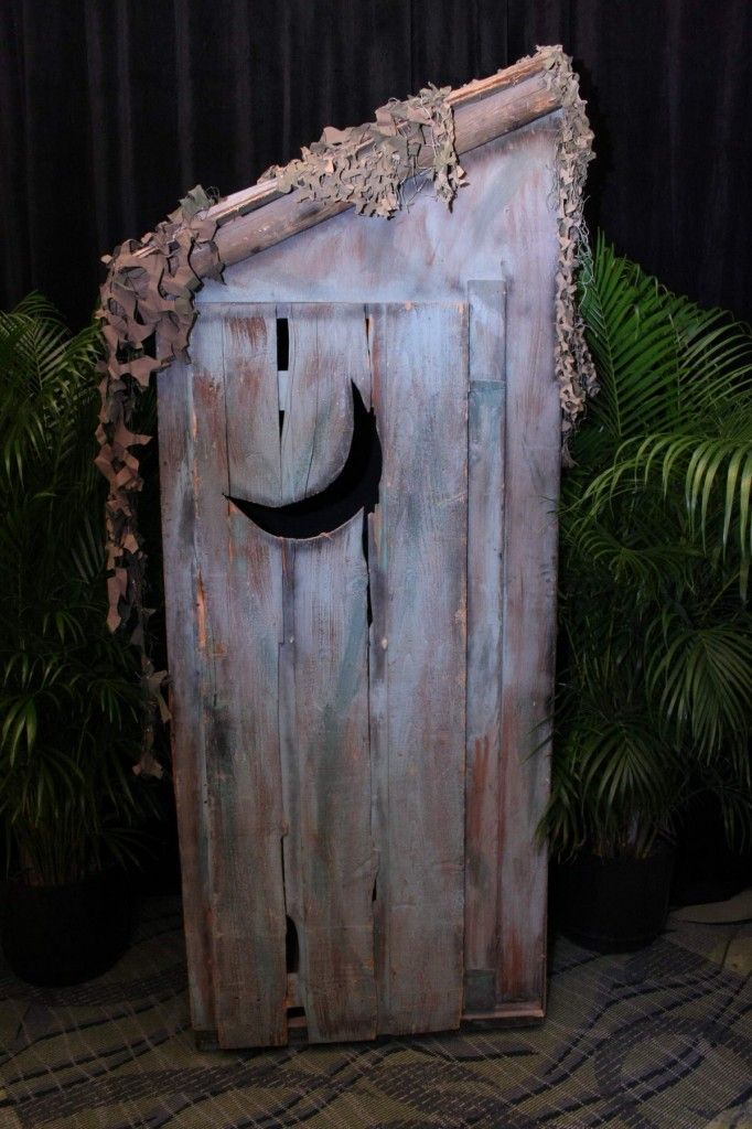 an old wooden door with a black moon on it's face and some plants in the background