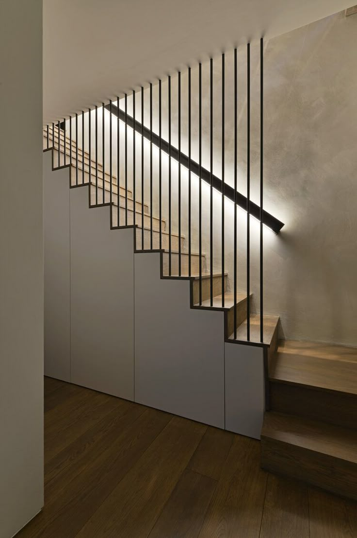 a wooden staircase with metal handrails next to a white wall and wood flooring