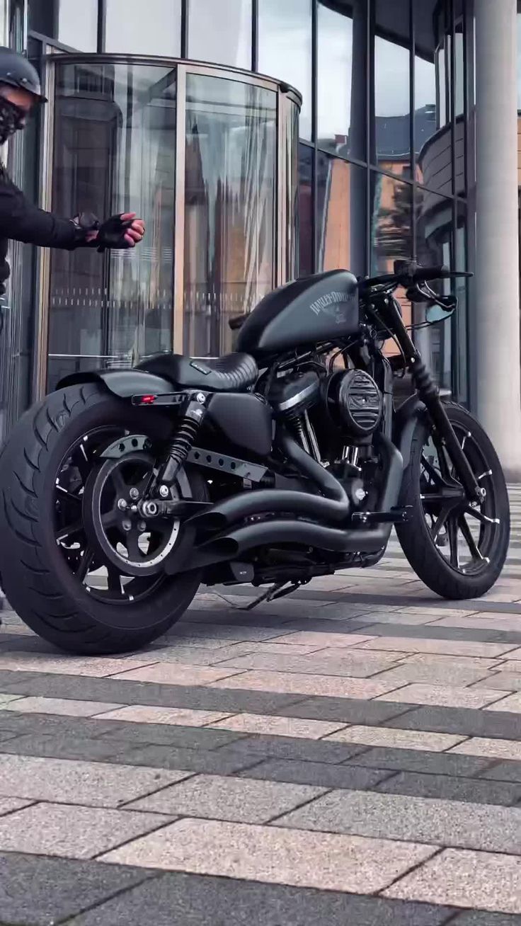 a man standing next to a black motorcycle on a brick sidewalk in front of a building