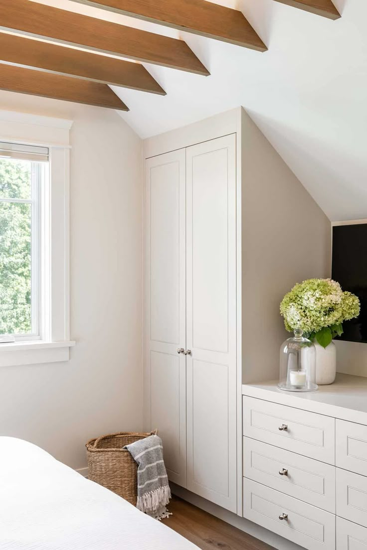 a bedroom with white cupboards and drawers next to a window in an atticed room