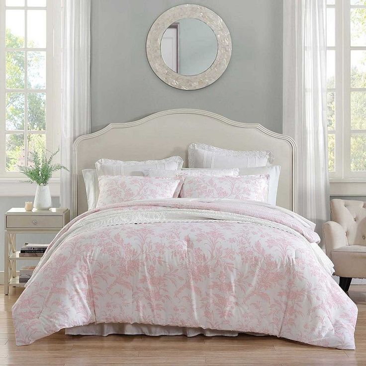 a bed with pink and white comforters in a bedroom next to a mirror on the wall