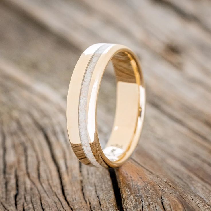 a gold wedding ring with white marble inlays sits on a piece of wood