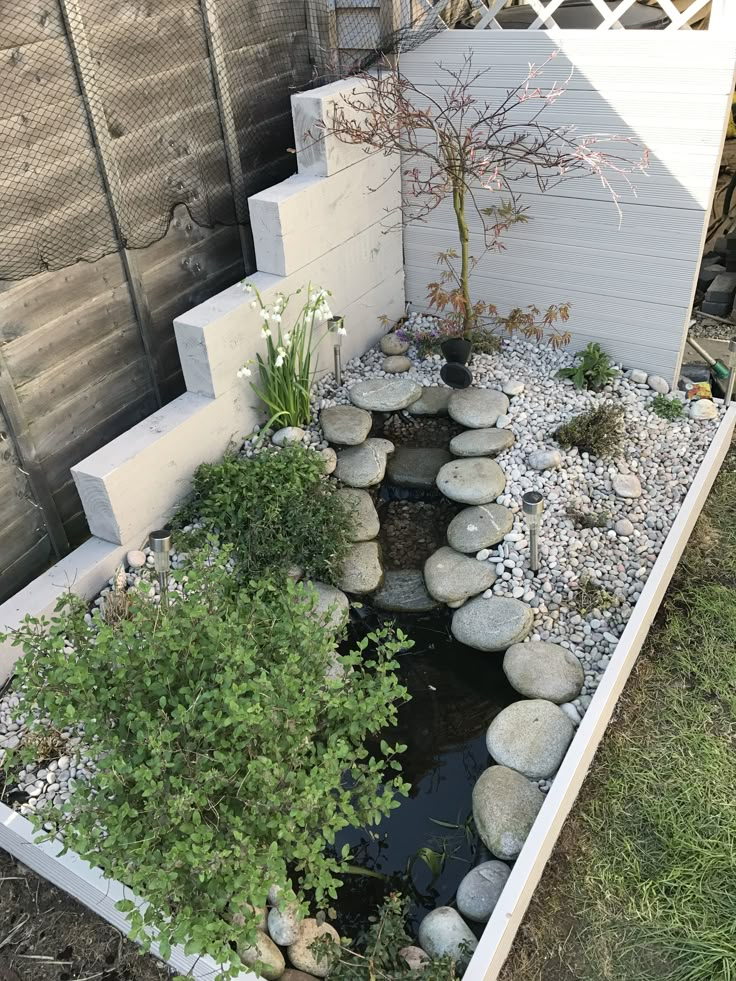 a small garden with rocks and plants in the center, along side a white fence