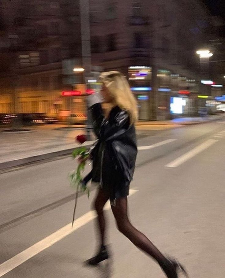 a woman walking down the street with a bouquet of flowers in her hand and wearing black boots