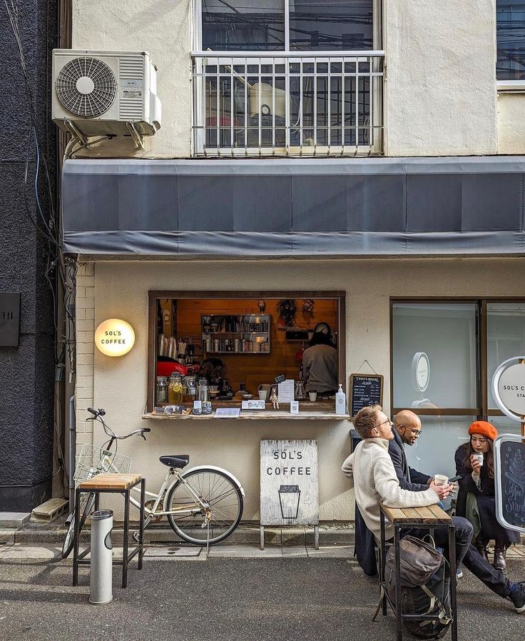 three people sitting at a table in front of a coffee shop with bikes parked outside