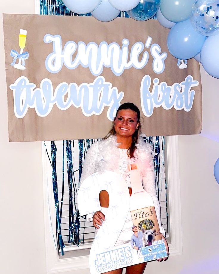 a woman standing in front of a sign with balloons around her and holding a book