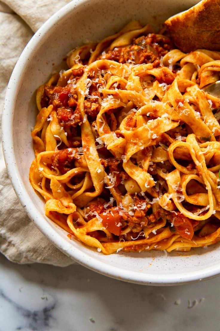 a white bowl filled with pasta and sauce on top of a marble counter next to a wooden spoon