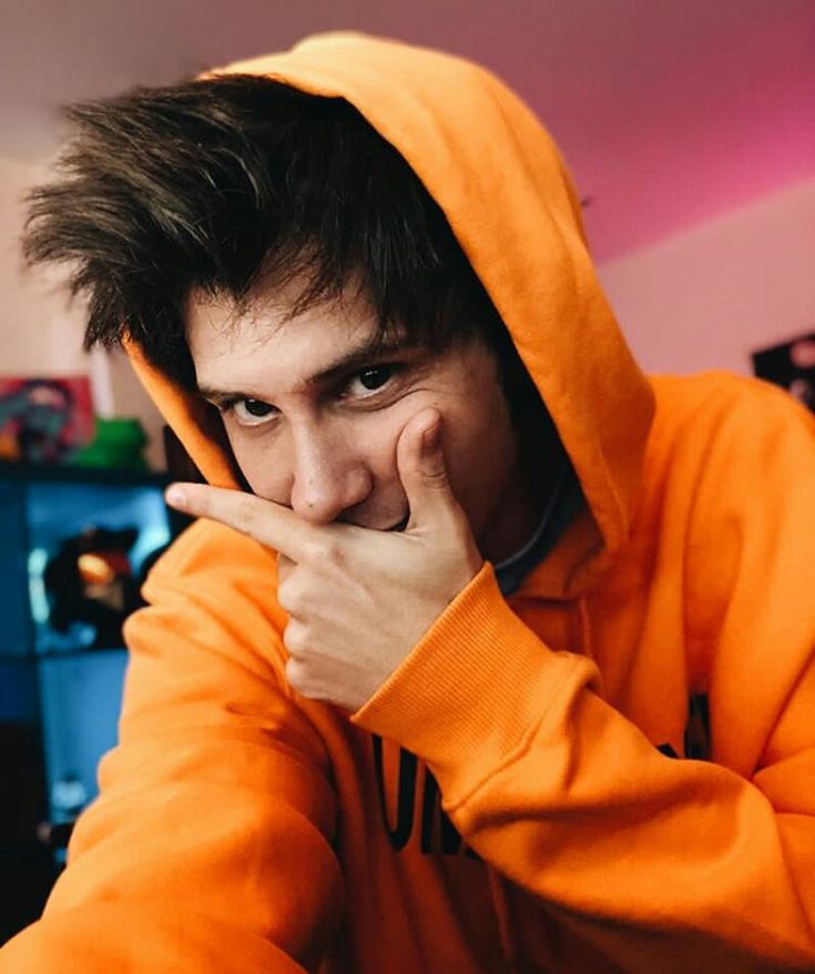 a man in an orange hoodie with his hand under his chin and looking at the camera