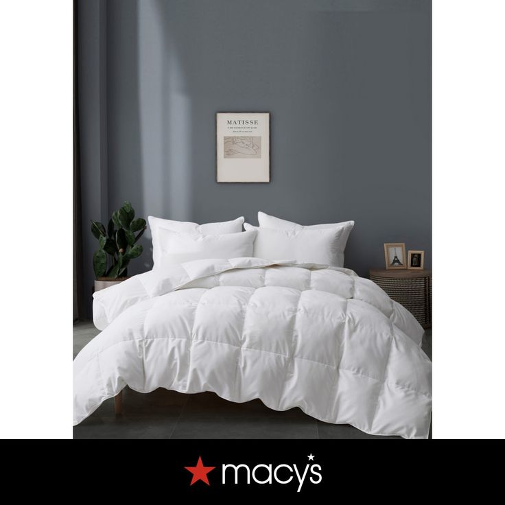 a white comforter on a bed in a room with gray walls and a plant