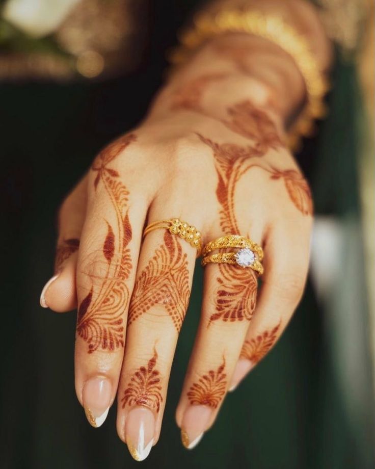 a woman's hand with henna tattoos and gold rings on her left hand