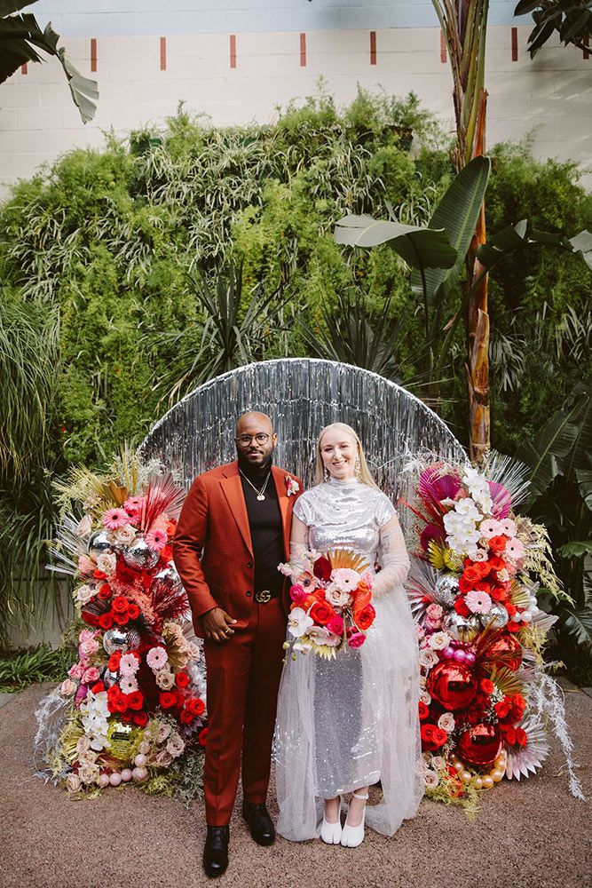 a man and woman standing next to each other in front of a floral display with red flowers