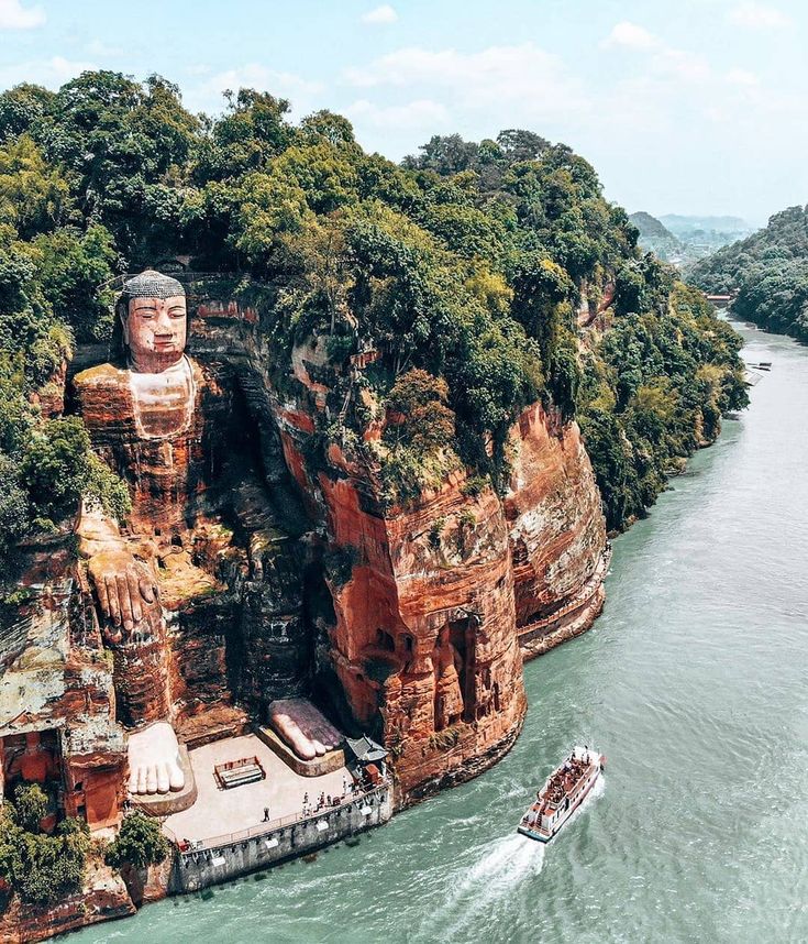 an aerial view of a boat traveling through the water next to a giant buddha statue