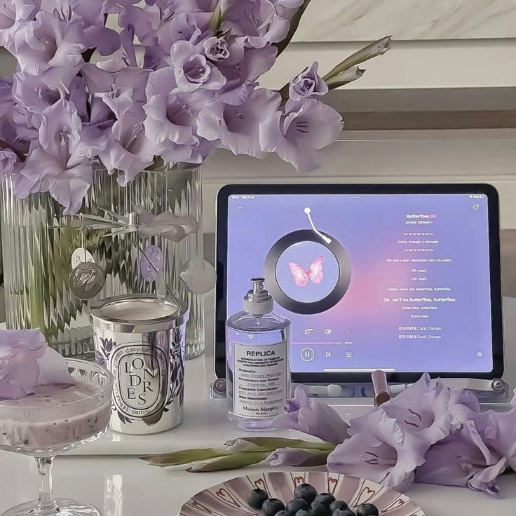 purple flowers are in vases next to a computer screen and other items on a table