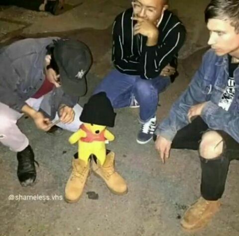 three young men sitting next to each other in front of a stuffed animal toy on the ground