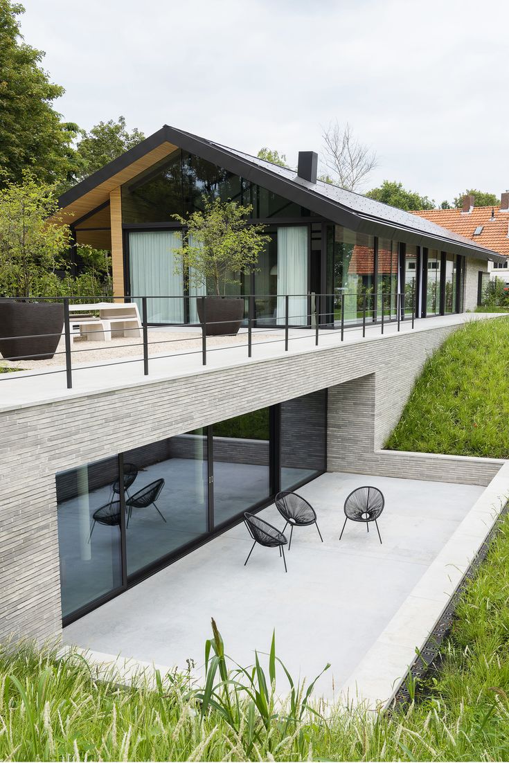 an outdoor patio with chairs and tables in front of a modern house on the hillside